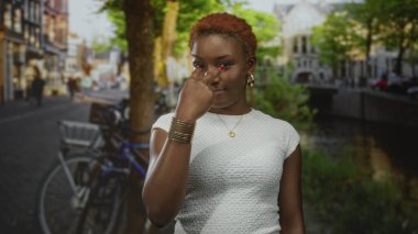 Kadın kaldırım taşı caddesindeki bisiklet ve tarihi binalarla dolu bir kanalda kamerayı işaret ediyor; özgüven azmi güçlendirme.