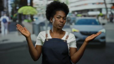 Önlük giymiş bir kadın hareketli bir şehir caddesinde kendinden emin duruyor, gücünü ve modern şehir yaşam tarzını aktarıyor..