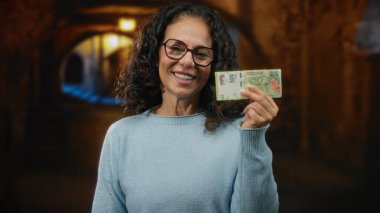 Bir şehir caddesinde elinde Arjantin pezosu tutarken gülümseyen bir kadın, canlı bir fon ile finansal temalar sergiliyor..