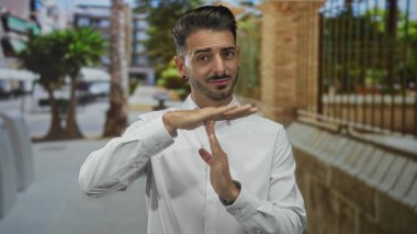 Latin kökenli genç adam, şehir caddesinde palmiye ağaçlarıyla kaplı bir jest yaparken ellerini gösteriyor..