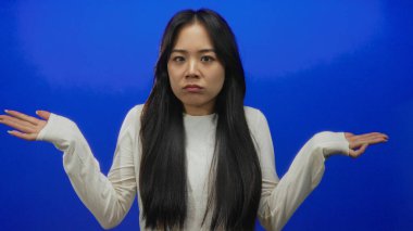 Belirsizliğini ifade eden, elleri mavi arka plan duvarında beyaz gömlek ve uzun saç giyen, kafa karıştıran ya da duyguları sorgulayan bir kadın..