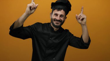 Siyah üniformalı İspanyol erkek şef turuncu bir arka plana sevinçle bakıyor..