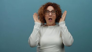 Kıvırcık saçlı, gözlerini kapayan, gülümseyen, gözlüklü, mavi arka planda yaşayan, soyutlanmış, orta yaşlı İspanyol asıllı bir kadın..