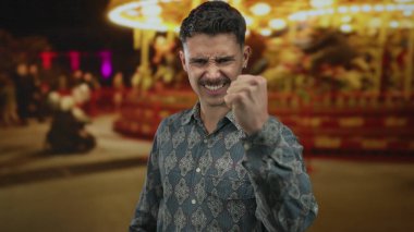 Fonda bulanık ışıklar olan canlı bir panayırda kararlı bir ifadeye sahip genç adam, gündelik ama yoğun bir odak ve enerji anı yakalıyor..