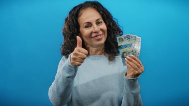 Gülümseyen kadın, Avustralya dolarlarını tutuyor. Mavi duvara başparmak işareti yapıyor. Finansal başarı fikrini gösteriyor..