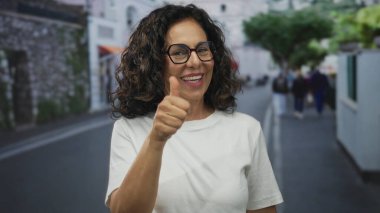 Orta yaşlı İspanyol kadın, bir şehir caddesinde ürün sunarken ellerini açık gösterdi; onay iyimserliği.