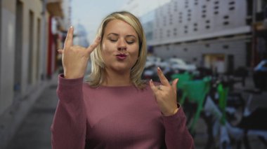 Kadın çıplak elle sokak sahnesinde arkası bulanık binalarla kaya boynuzları hareketi yapıyor..