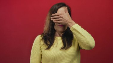 Kadın, parlak kırmızı arka planda el ele tutuşmuş sarı süveter giyiyor. Tecrit edilmiş ortamda gizem ve entrika olduğunu söylüyor..