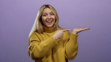 Sarı kazaklı kadın açık avucunu işaret ediyor. Mor arka plana karşı neşeli bir yüz ifadesiyle sunum potansiyelini ve dostça iletişimi vurguluyor..