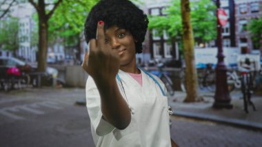 Laboratuvar önlüğü giyen kadın doktor ve steteskop şehir sokaklarında orta parmak gösteriyor..