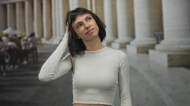 Bir binanın mermer sütunlarına bakarken saçlarına çıplak göbeğiyle dokunan kadın; sessiz tefekkür.