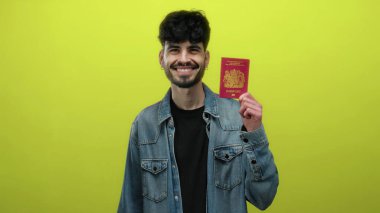 Elinde İngiliz pasaportu olan gülümseyen bir adam canlı sarı arka plana karşı izole edilmiş. Kimlik ve seyahat için hazır..