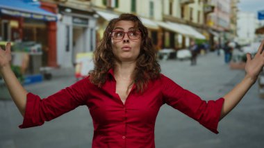 Şehir caddesinde hareketli hareketli bir kadın, açık gökyüzünün altında gözlük ve kırmızı tişört giyiyor, arka planda bulanıklık var, şehir ortamında gün içinde duygularını dışa vuruyor..
