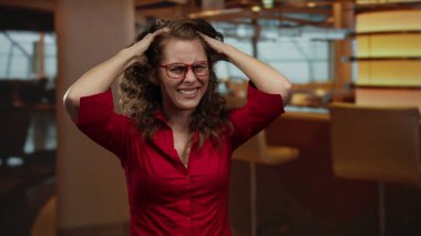 Restoranda elleri başının üstünde kırmızı gömlek ve gözlük takan bir kadın kafeteryada hayal kırıklığı yaşıyor..