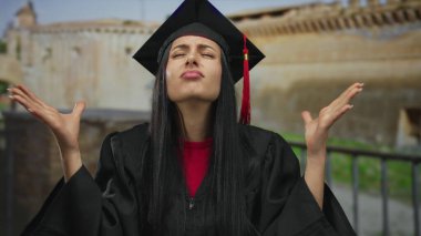 Şapkalı ve cüppeli genç İspanyol kadın mezuniyet töreninden sonra hayal kırıklığını arka planda antik mimariyle gösteriyor..