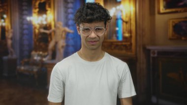 Gözlüklü genç adam tarihi galeri binasında mermer heykelin yanında burun büküyor..