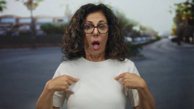 Şaşırmış yüz ifadesi olan bir kadın, bulanık bir geçmişi ve parlak bir günışığı olan, duygularını ve merakını ifade eden bir sokakta kendini işaret ediyor..