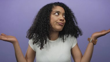 Kıvırcık saçlı bir kadın mor stüdyoda başını eğerken avuçlarını silker..