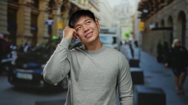 Gri kazaklı genç Çinli adamın taksilerle ve arka planda insanlarla dolu bir caddede parlak bir fikri var..