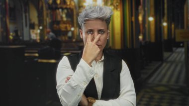 Kilisenin loş bir binasında boğazını kesen bir kadın. Kilise sıraları ve sütunlarıyla çerçevelenmiş. Öfke..