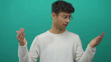 Gözlüklü ve beyaz tişörtlü bir adam, bir sette şaşkın bir ifadeyle omuz silkiyor; belirsizlik.