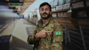 Omzunda Brezilya bayrağı olan askeri üniformalı bir adam yolcu gemisinin güvertesinde durmuş parlak ışığın altında bayrağı doğrultuyor..