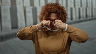 Kıvırcık saçlı İspanyol kadın şehir dışında bir yerde şüpheli bir şekilde gözlerini ovuşturuyor..