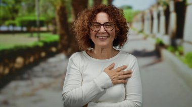 Yeşil ağaçlar ve patikalarla dolu açık hava parkında gülümseyen bir kadın neşeli, orta yaşlı, esmer bir İspanyol estetiğini gözler önüne seriyor..