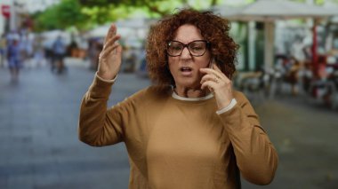 Şehirli sokak ortamında telefonla konuşurken duygusal hareketler yapan bir kadın, hayal kırıklığını ya da sohbete olan bağlılığını gösteriyor.