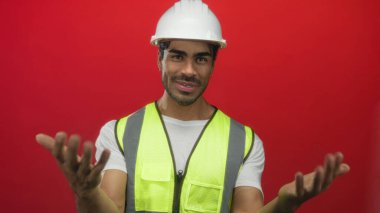 Erkek mühendis kırmızı stüdyoda beyaz bir şapka ve hoş geldin pozu veren neon bir yelek giyerek el ele tutuşuyor..