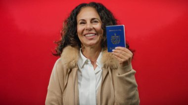 Orta yaşlı bir kadın kırmızı arka plana karşı Küba pasaportu taşıyor, neşeli bir ifadeyle seyahat ve kimlik sergiliyor.
