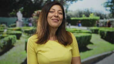 Taştan heykelin yanındaki yeşil bir parkta manikürlü çitlerin yanında gülümseyen orta yaşlı kadın, huzur huzur, neşe ve barış..