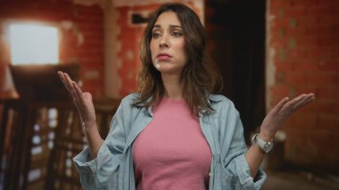 İnşaat alanındaki İspanyol kadın pembe gömlekli mavi ceketli, belirsiz bir ifadeyle gündüz vakti şehir merkezindeki tamamlanmamış bina geçmişini sorguluyor..