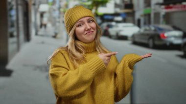 Sarı kazak ve şapkalı bir kadın, bir şehir caddesini işaret ediyor, canlı bir şehir manzarasında şehir yaşamını gözler önüne seriyor..