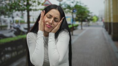 Latin kökenli genç bir kadın şehir sokaklarında stresli görünüyor, ağaçların ve binaların arasında el ele tutuşuyor, kent stresi ve duygularını paylaşıyor..