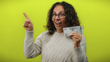 Uae 'den orta yaşlı bir kadın Dirham banknotunu tutarken izole edilmiş sarı arka plana şaşırmış görünüyor..