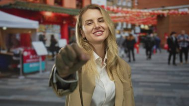 Fenerlerin altında gülümseyen kadın, bulanık insanlar ve kırmızı çadırlar ile çevrili kameraya doğru şakacı bir şekilde uzanıyor..