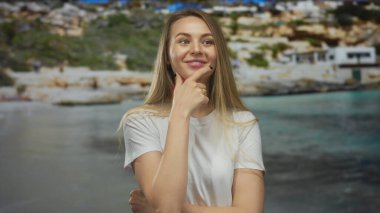 Arka planda bulanık deniz manzaralı, manzaralı bir plajda mutlu bir şekilde el kol hareketi yapan genç kadın rahat açık hava keyfi ve pozitifliğini sergiliyor..