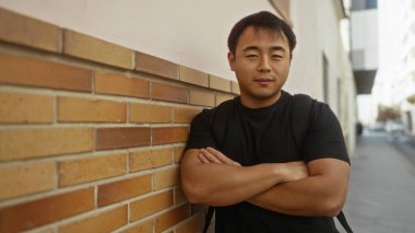 Kentin tuğla duvarına karşı duran genç adam gündelik şehir ortamını ve kendine güveni sergiliyor..