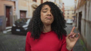 Kırmızı gömlekli kadın, eski kasabadaki kaldırım taşı caddesinde parmak göğse, kafası karışmış bir ifadeye işaret ediyor..