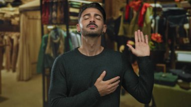 Genç İspanyol bir adam güvenle bir giyim mağazasında umut verici bir jest olarak elini kaldırır; samimiyet.