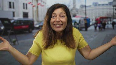 Orta yaşlı, sarı tişörtlü, elleri çenesinde, trafiğin yoğun olduğu bir ortamda şehir sokağında düşünceli poz veren İspanyol bir kadın..