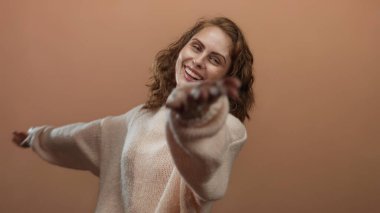 Sevinçle gülümseyen bir kadın kollarını minimalist kahverengi arkaplana açıyor mutluluk ve özgürlüğü ifade ediyor..