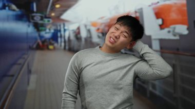 Şaşırmış bir ifadeye sahip genç bir adam, açık deniz manzarası ile çevrili bir yolcu teknesinde duruyor, canlı bir gemi teçhizatı ve yapılara karşı düşünceli bir görünüm sergiliyor.