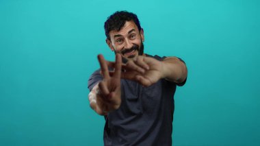 Sakallı İspanyol bir adam, gülümsüyor ve parlak mavi arka plana karşı hashtag işareti yapıyor..