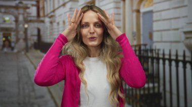 Kadın, genç bir sarışının olduğu bir sokakta sokak gösterisinde el ele tutuşuyor. Dost canlısı bir jest yapıyor ve kentin arka planında gülümsüyor..