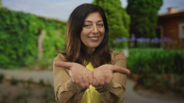 İspanyol orta yaşlı kadın, açık avuçlarını parlak güneş ışığı ve yemyeşil yaprakların altında tutuyor..