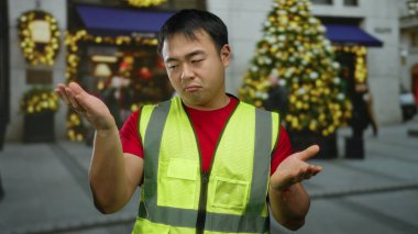 Yansıtıcı yelek giyen bir adam festival süslemeleri ile caddelerde omuz silkiyor, şehir merkezinde gündüz kafa karışıklığını ifade ediyor..