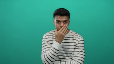 Çizgili genç adam yeşil arka plana şaşırmış görünüyor, izole edilmiş bir portre ortamında gizemli bir şekilde modern ve temiz bir stil sergiliyor..