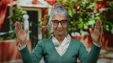 Canlı bir sokak arkaplanında el hareketleriyle gri saçlı yaşlı bir kadın şehir ortamında kendine güven ve dışavurumculuk gösteriyor..
